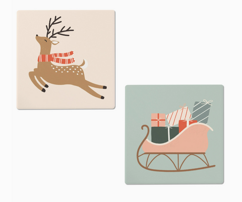 Two Christmas-themed ceramic coasters: a deer with a scarf and a sleigh with presents on a light blue background.